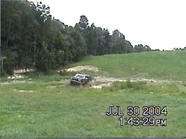 Dark SUV driving through a muddy field with trees in the background