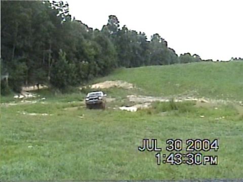 1988 Ford Bronco - Truck navigates off-road terrain with a wooded area behind it. Timestamp indicates July 30, 2004.