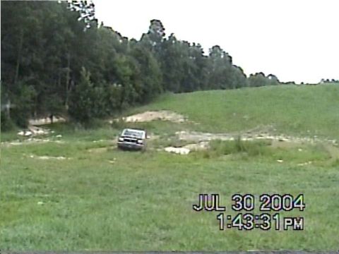 1988 Ford Bronco - A vehicle navigates a grassy, off-road terrain with a wooded area visible in the distance.