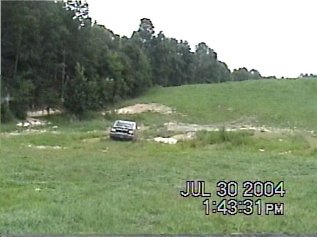 SUV driving through a muddy field with trees in background. Date stamp shows July 30, 2004