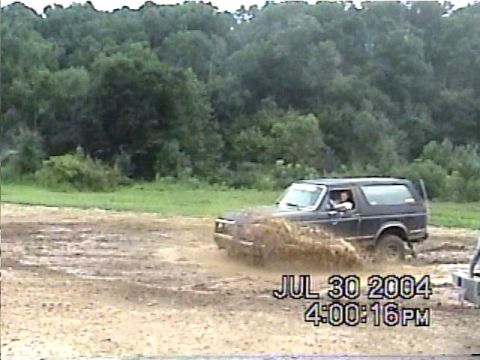 1988 Ford Bronco - A dark SUV navigates a muddy terrain, kicking up water and splashing water.