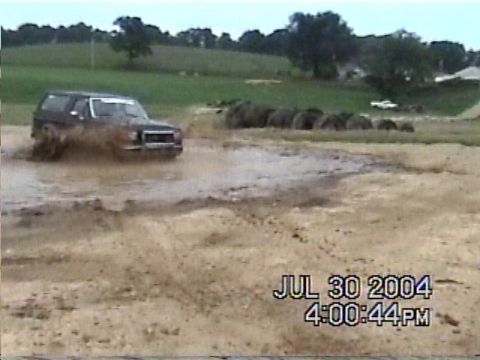 1988 Ford Bronco - A dark SUV navigates a muddy terrain, kicking up water and dirt. The timestamp indicates the event occurred on July 30, 2004.