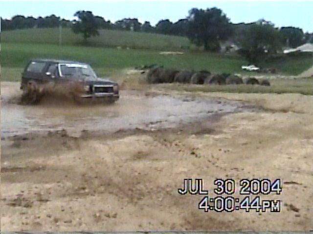 Dark SUV splashing through mud, front view. Date stamp shows July 30, 2004