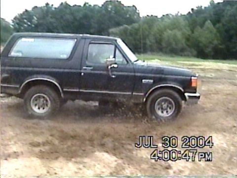 1988 Ford Bronco - 1988 Ford Bronco driving through a muddy area with trees in the background. Date stamp visible.