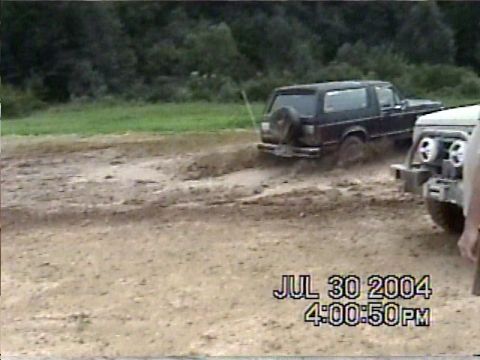 1988 Ford Bronco - Two off-road vehicles navigate a muddy terrain, with one SUV kicking up dirt as it moves.