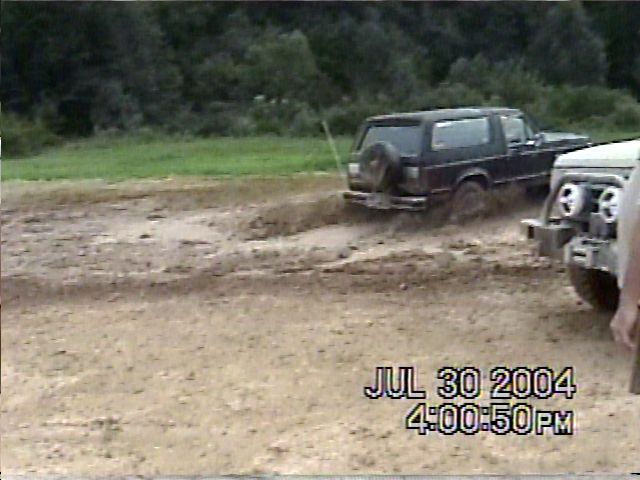 Two off-road vehicles driving through mud. One is a dark SUV with a spare tire on the back