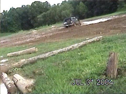 1988 Ford Bronco - A dark SUV navigates a muddy off-road course with several logs visible in the foreground.