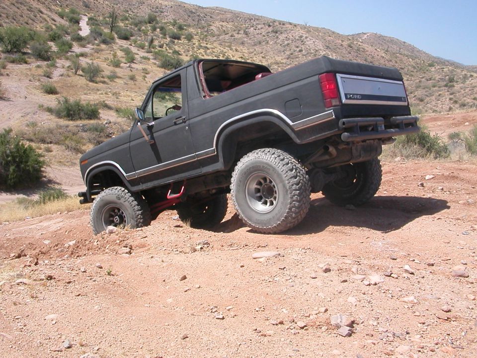 Black lifted Ford Bronco with removed front roof on big off-road tires descending a desert dirt hill