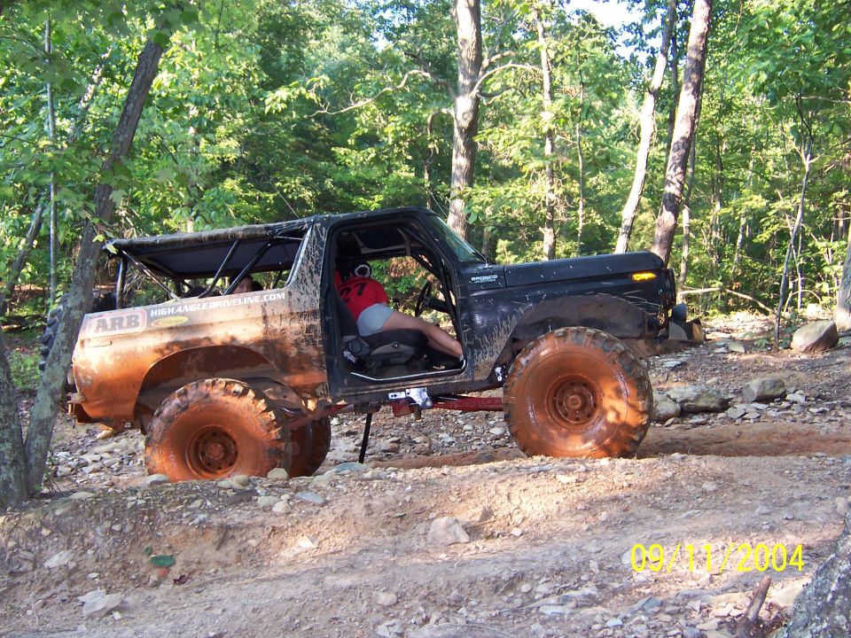 Muddy doorless Ford Bronco with roll cage climbing rocky trail on oversized tires