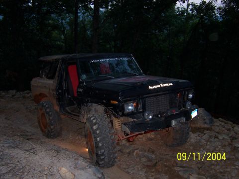 1978 Ford Bronco - Mud-caked black full-size Ford Bronco posed three-quarter front on a rocky trail at dusk, wearing "Alaskan Extreme" hood lettering and an A…