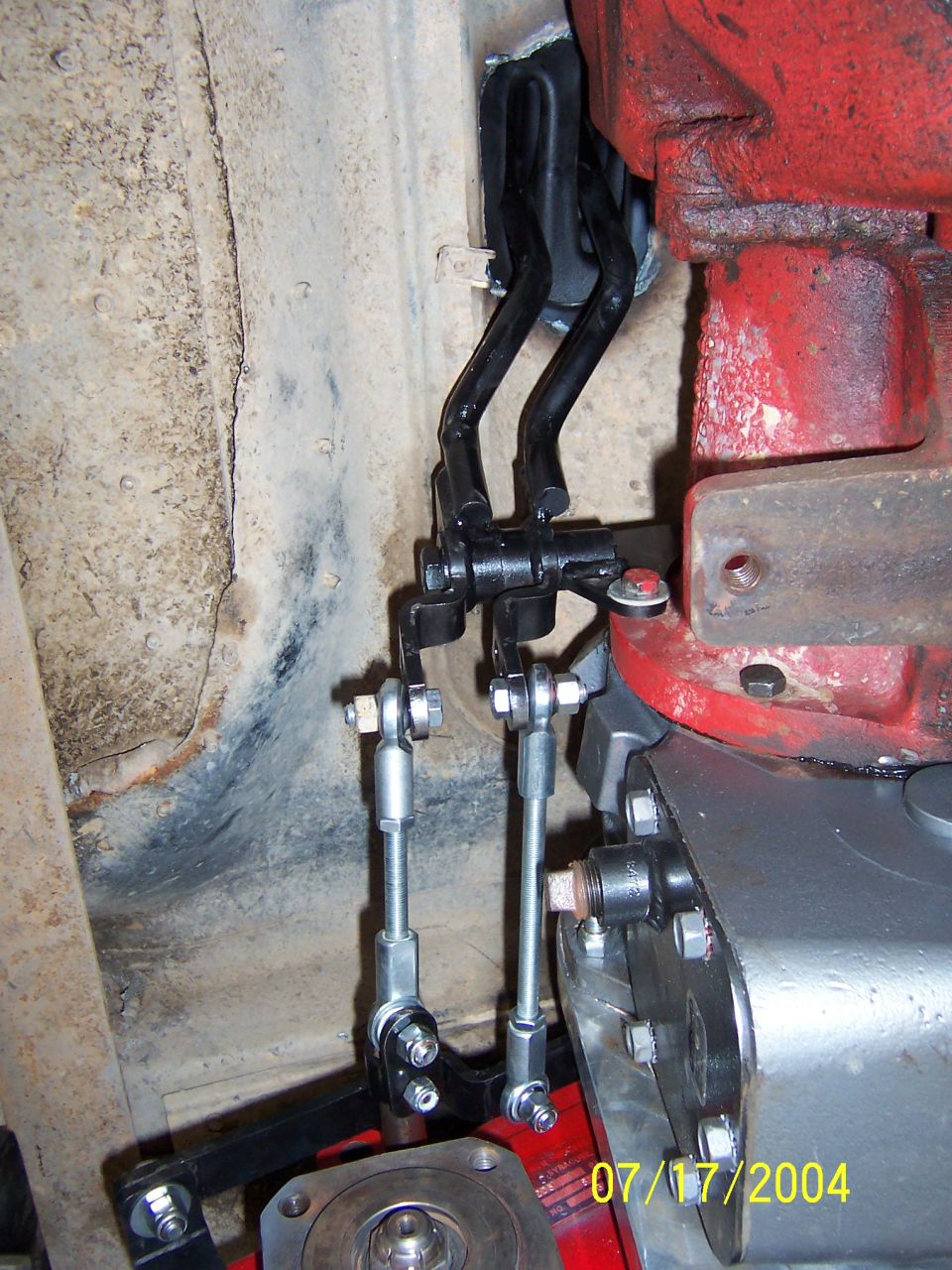 Close-up of a vehicle's transmission linkage with rods and levers connected to a red component