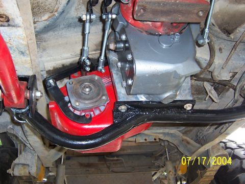1978 Ford Bronco - Underbody close-up of a freshly painted red transmission bolted to a bare aluminum-finish transfer case, dated 07/17/2004. A round bolt-on…