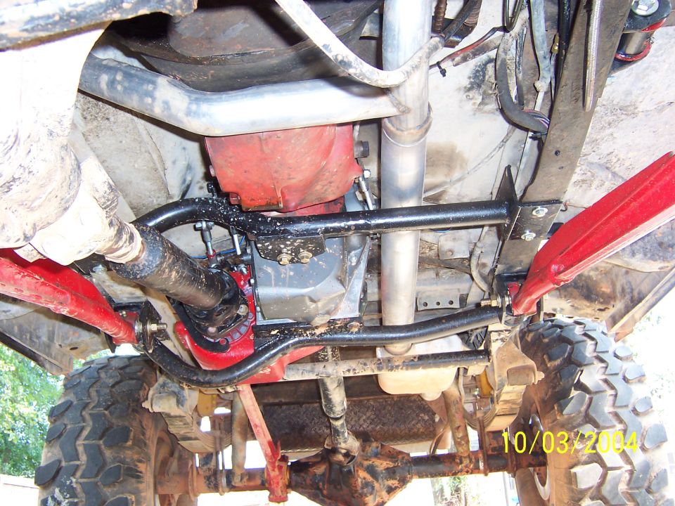 Underbody of lifted 4x4 showing red transfer case, black skid crossmember and driveshaft