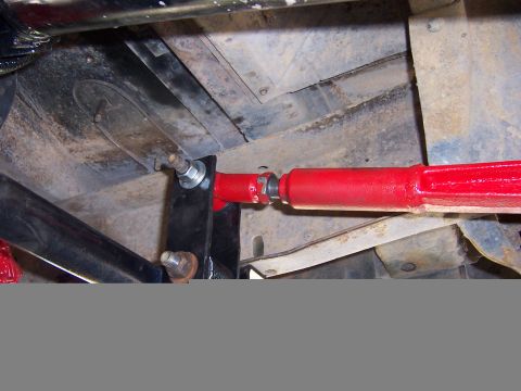 1978 Ford Bronco - Underbody view of a red-painted adjustable rod with a threaded end and jam nut, resembling a track bar or steering link, bolted to a black…
