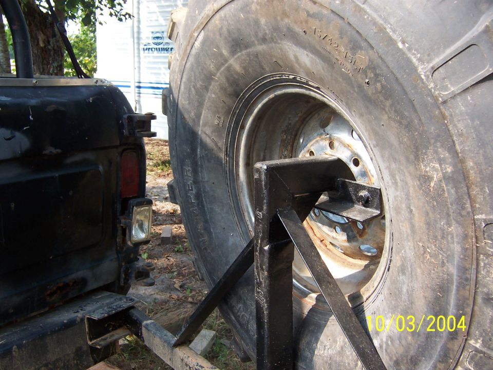 Close-up of a large spare tire mounted on a carrier attached to the rear of a black vehicle