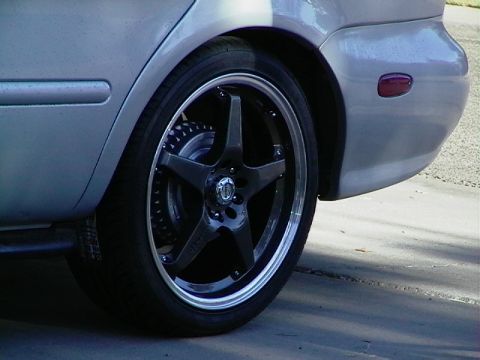 1999 Ford Taurus - Custom rims fitted to the rear wheel of a silver car, showing the fender and part of the bumper.