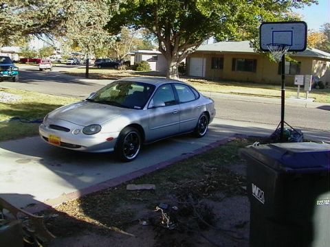 1999 Ford Taurus - A silver sedan is parked on a concrete driveway in front of a house.