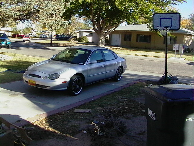 Silver sedan parked in a driveway next to a trash can and basketball hoop