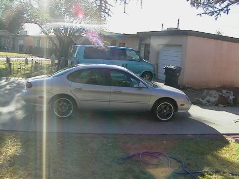 1999 Ford Taurus - A silver 1999 Ford Taurus sedan is parked in a driveway next to a blue van.