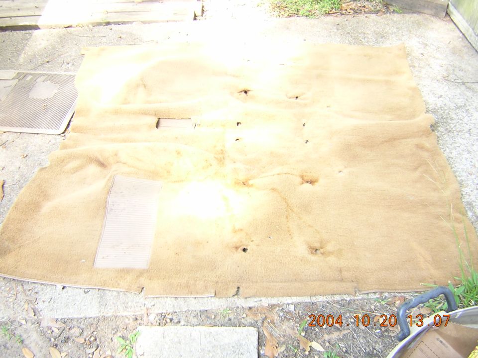 Tan automotive carpet laid out on a concrete pad outdoors, sun-faded with cut holes