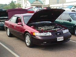 1995 Ford Taurus - Maroon 1995 Ford Taurus with hood and trunk open, parked outdoors with other vehicles.