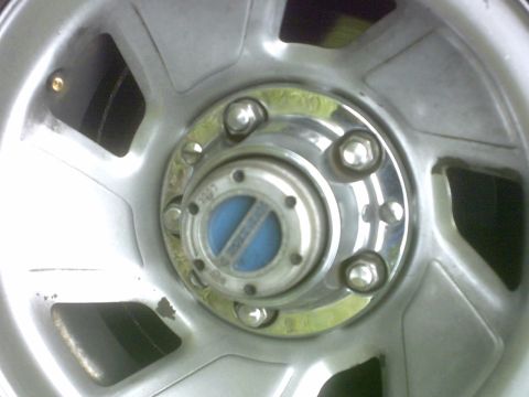 1992 Ford Bronco - Close-up of a silver alloy wheel a blue and chrome hubcap with visible text and the Supermotors.net logo.