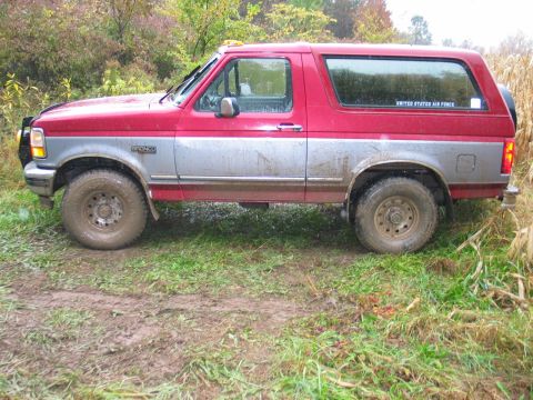 1995 Ford Bronco - This two-tone red and silver Ford Bronco is parked off-road in a rural setting.