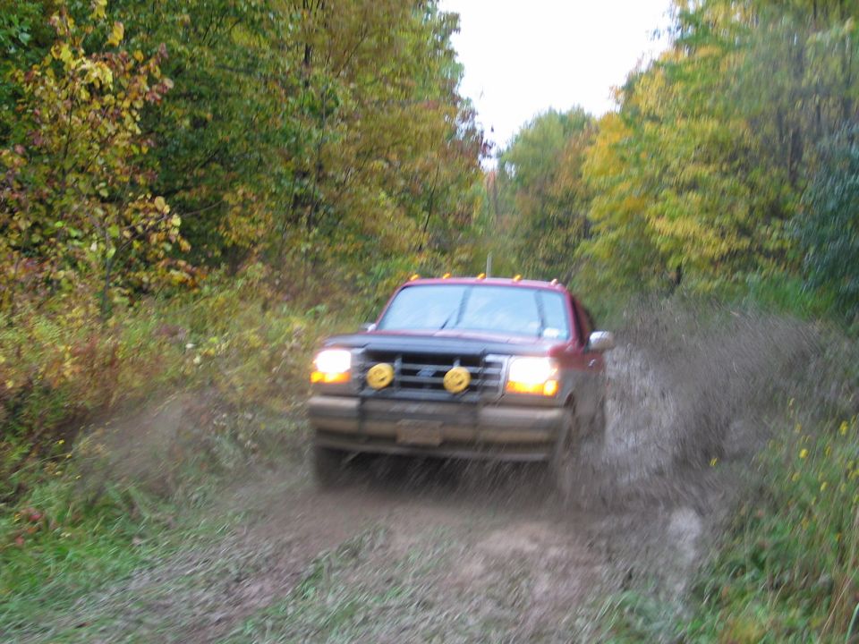 Red Ford SUV with brush guard and yellow lights splashing mud on a fall trail