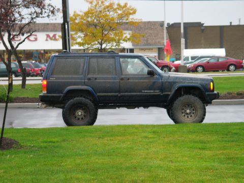 1995 Ford Bronco - A dark blue Jeep Cherokee XJ is parked on the side of the road with a store in the background.