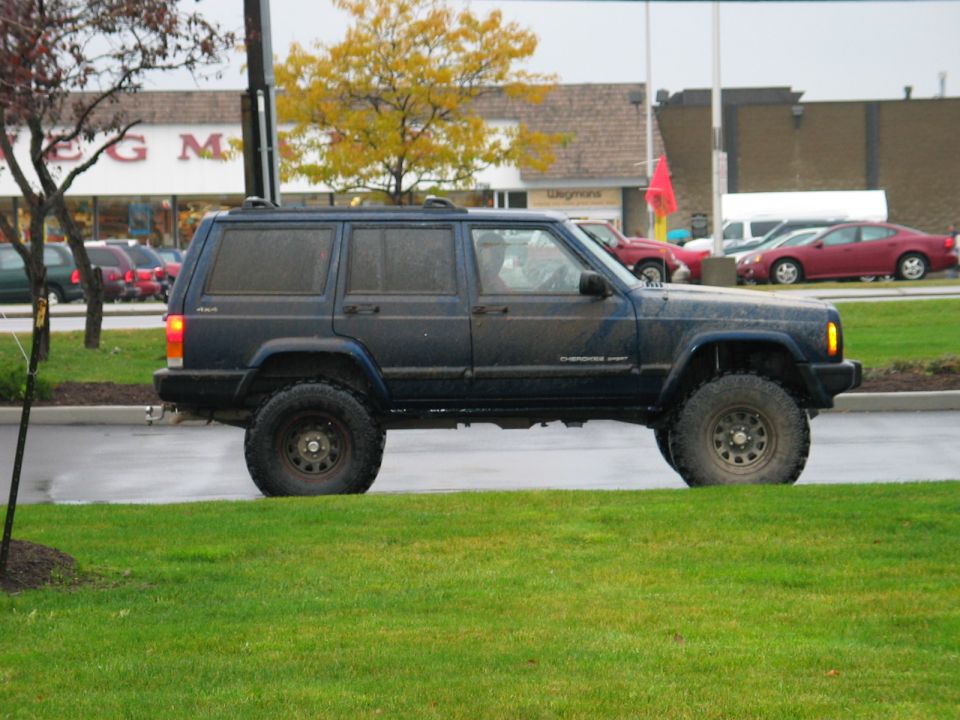Lifted mud-flecked dark blue Jeep Cherokee Sport in side view in a wet parking lot