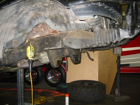 1992 Ford Bronco - Underside front view of a truck on jack stands with the front axle and suspension removed, leaving bare frame rails, crossmember, empty whe…