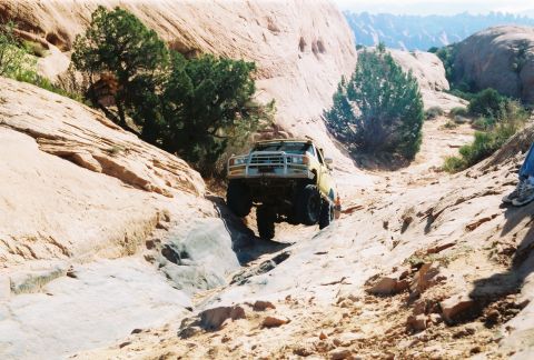 1996 Ford Bronco - An off-road vehicle navigates a challenging path through a desert landscape with large rock formations.
