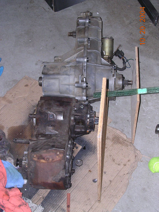 Transmission and transfer case assembly on cardboard with wooden supports. Date stamp 10.20.2004 visible
