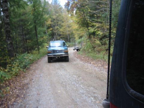 1996 Ford Bronco - A teal Ford Bronco drives down a gravel road surrounded by trees in the fall.