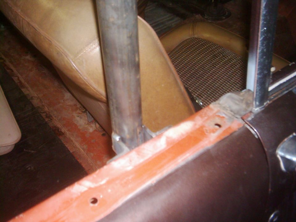 Vehicle interior showing tan seats, a metal roll cage post, and orange painted metalwork