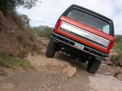 1984 Ford Bronco - This Ford Bronco navigates a challenging off-road trail with a rocky incline.