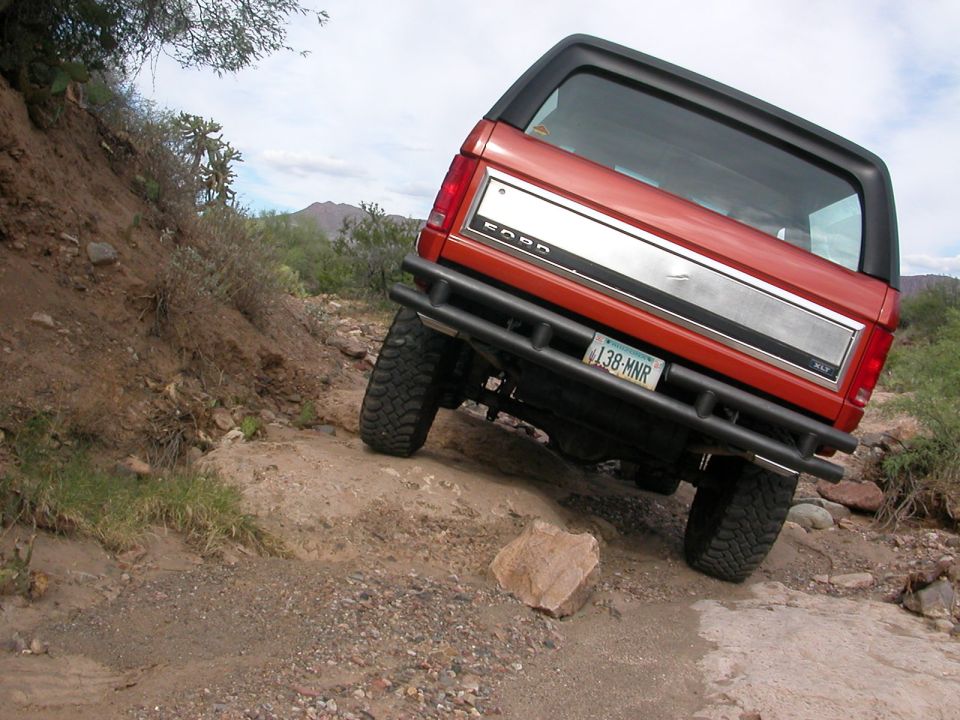 Orange Ford Bronco with black top and aftermarket bumper on rocky terrain
