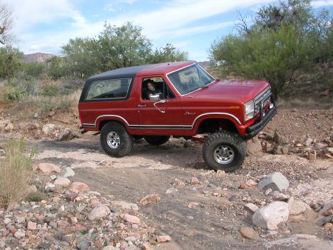 1984 Ford Bronco - This red 1984 Ford Bronco with a black top navigates a rocky, off-road trail.