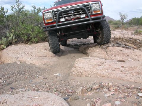 1984 Ford Bronco - This red Ford truck navigates a rocky, off-road trail with a clear blue sky overhead.
