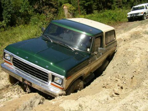 1978 Ford Bronco - A green and tan 1978 Ford Bronco navigates a muddy trail, with another white SUV visible in the background.