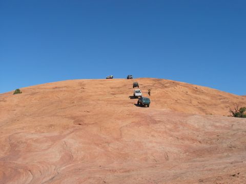 1993 Ford Bronco - Multiple SUVs and trucks navigate a steep, sandy hill on an off-road trail.