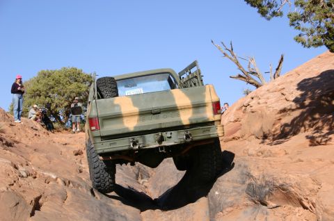 1993 Ford Bronco - A camouflaged pickup truck navigates a challenging off-road trail in a desert landscape.