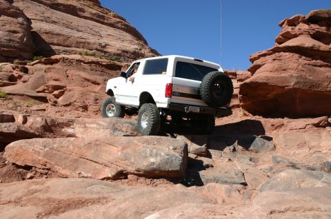 1993 Ford Bronco - A white 1993 Ford Bronco navigates a challenging off-road course through a rocky canyon.