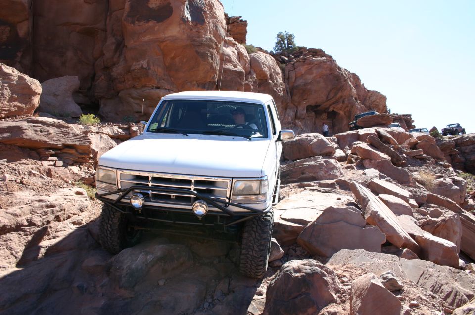 White SUV navigating a steep, rocky trail with other vehicles visible in the background