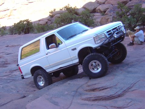 1993 Ford Bronco - A white Ford Bronco navigates a rocky trail with a person and dog watching.