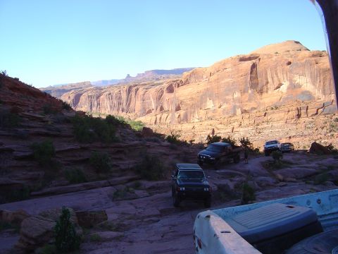 1993 Ford Bronco - Several off-road vehicles navigate a trail through a scenic canyon landscape under a clear blue sky.