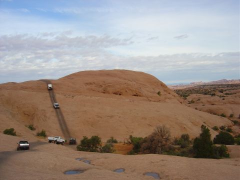 1993 Ford Bronco - Multiple off-road vehicles navigate a challenging dirt path on a desert landscape.