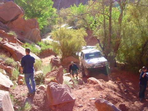 1993 Ford Bronco - Two SUVs traverse a challenging off-road path through a canyon with sparse vegetation.