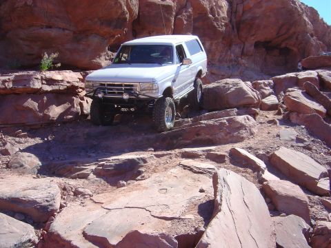 1993 Ford Bronco - This white SUV is equipped for off-road adventures, tackling a challenging rocky path.