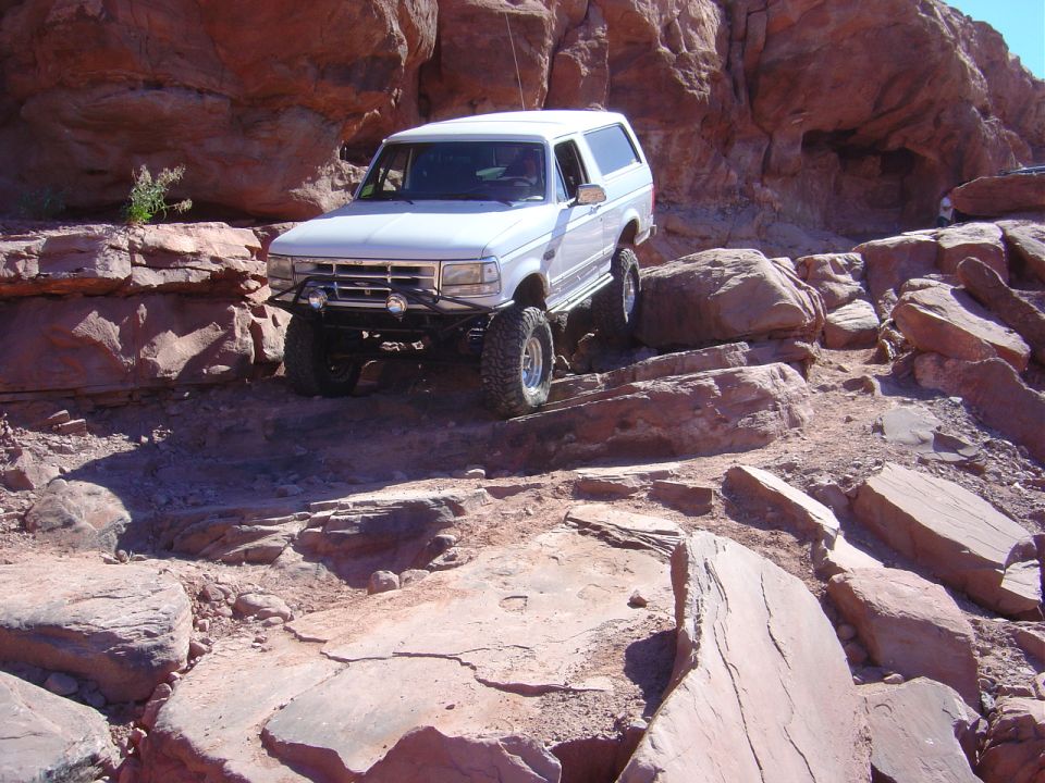 White lifted Ford Bronco crawling down red sandstone ledges on a desert rock trail